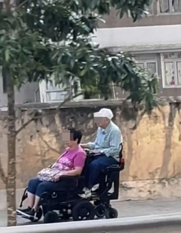 Elderly couple on dual electric wheelchair at speed on pedestrian slope